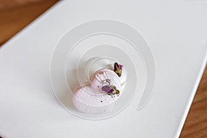 A white heart-shape cake lies on a white plate on a light background. Light macaroons. Delicious pastries