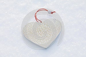 White heart-shaped toy with small cracks in the snow, template for designer