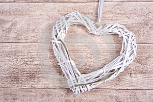 White heart from wickerwork with grass on wooden background