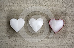 White hearts made of snow with one red colored cookie cutter laying on concrete background surface. Flat lay, Top view.