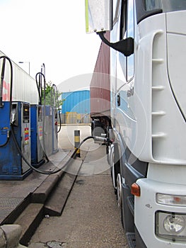 White heavy truck filling up with diesel at a commercial fuel pump with a brown shipping container trailer