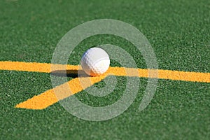 White hockey ball on a green astroturf pitch.