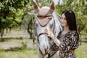 White horse adorned with crochet ear net being caressed by woman outdoors