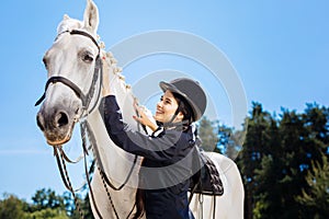 Appealing horsewoman smiling while looking at her gentle white horse