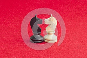 White horse and black horse, traditionally confronted in chess game, have reconciled. Image in red background