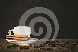 White hot cup of coffee and sticks of cinnamon/white hot cup of coffee and sticks cinnamon on a dark wooden background. Copy space