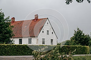 White house with orange roof tiles beyond green hedge in rural setting on rainy day in SkÃ¥ne Scania Sweden