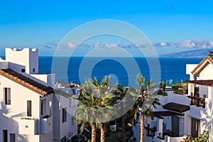 White houses among palm trees overlooking the Atlantic Ocean and La Gomera island against the blue sky photo