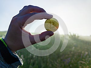 White human hand holding a Bitcoin shiner on a morning grassy meadow background photo