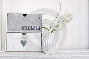 White hyacinth in a vase next to small chest of drawers with the inscription Love. boho house