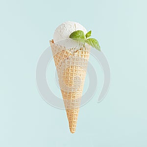 White ice cream cone scoop in waffle cone with mint leaf on soft light pastel green background, closeup, square.