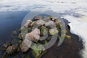 White ice and snow pieces with several stones in river coast water in cold winter morning