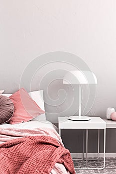 White industrial lamp on nightstand table next to king size bed with white bedding and pastel pink pillows and blanket