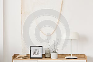 White industrial lamp, photo in frame and plant in pot on wooden console table in elegant living room with white wall