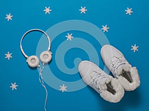 White insulated women`s winter sneakers on a blue background with snowflakes.