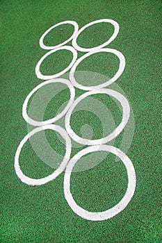 White interlacing circles on a rubberized green surface on a playground on a clear sunny day.