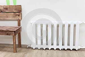 White iron radiator of central heating near wooden bench in room