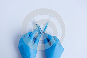 On white isolated background, hands of doctor in medical blue gloves hold an ampoule with syringe