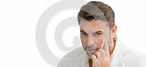 White isolated banner with copy space. Handsome serious man enjoy fresh perfect skin, applying facial cream. Portrait of