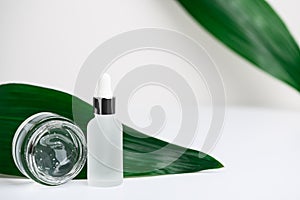 White jar with pipette with serum, transparent gel for the skin of the face on white background with fresh herbs. A