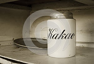A white jar for storage  cocoa with text `Kakao` in russian languige and an old metal tray with rust. Old white kitchen shelf. photo