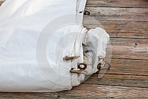 A white jib sail rolled up on the dock with shows a close up of the bolt rope and copper hanks