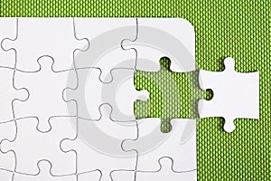 White jigsaw puzzle on green background, with one missing piece