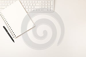 White keyboard and notepad on left side with black pen flat lay on white background.