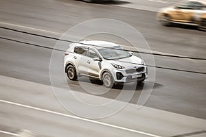 White Kia Sportage SUV car moving on city street. Front side aerial view of compact crossover on highway background