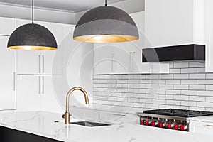 A white kitchen with a gold faucet and large pendant lights.