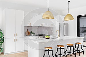 A white kitchen with gold lights, faucet, and hardware.