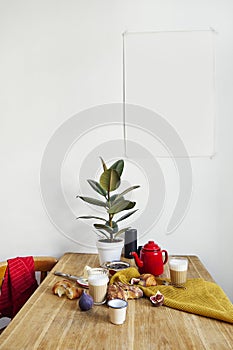 White kitchen interior with breakfast on wooden table, poster on the white wall, space for design layout.