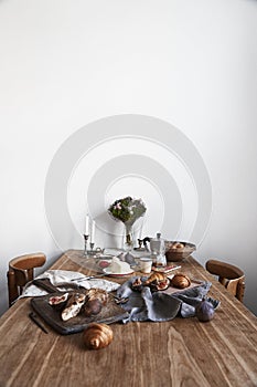 White kitchen interior with provence breakfast on wooden table, empty white wall, daylight.