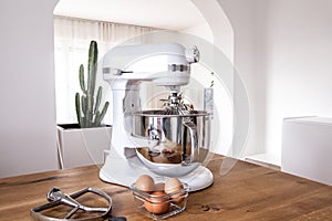 White kitchen machine and stand mixer on a wooden table in a bright design apartment