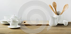 White kitchen utensils, dishware and other different white stuff for serving on white wooden board.