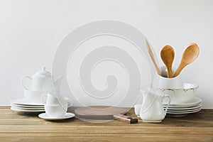 White kitchen utensils, dishware and other different white stuff for serving on white wooden board.