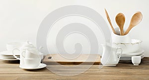 White kitchen utensils, dishware and other different white stuff for serving on white wooden board.