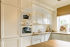 White kitchen wall with microwave and oven. Big window on the right wall