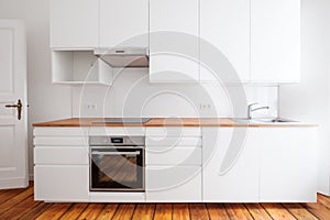 White kitchenette , newly built-in kitchen furniture frontal view with wooden worktop and board floor