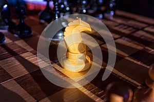 White knight staying against full set of black chess pieces. Closeup of chessboard with wooden pieces on table in sunlight, game