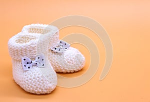 White knitted baby booties with bows on a delicate orange insulated background