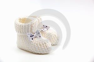 White knitted baby booties with bows on a gray isolated background