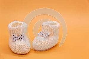 White knitted baby booties with bows on orange isolated background