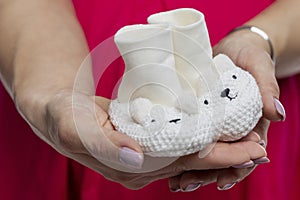 White knitted booties for a newborn in female hands. Close-up. Preparing for the birth of a baby