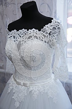 White lace wedding dress on a mannequin. Top part. Details of the bride`s attire at a wedding ceremony.