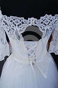 White lace wedding dress on a mannequin. Upper back. Clasp with pearls. Details of the bride`s attire at a wedding ceremony.