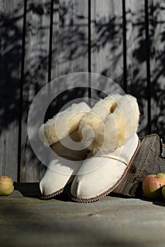 White lamb wool slippers houseshoes. On wooden table with apples. Keep your feet warm and cozy during the freezing cold season