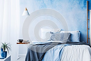 White lamp above table next to bed with blue and grey bedsheets