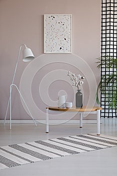 White lamp next to wooden coffee table with cotton flower in black vase, coffee cups and jug
