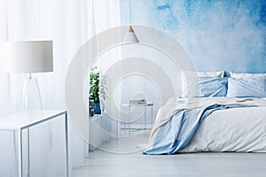 White lamp on a table in bright blue bedroom interior with bed a